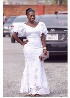 a woman wearing a white dress standing in front of a black car with her hands on her hips