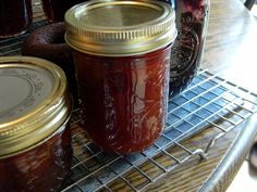 two jars filled with jam sitting on top of a metal rack next to other jars