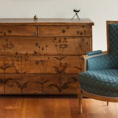 a blue chair sitting next to a wooden dresser on top of a hard wood floor