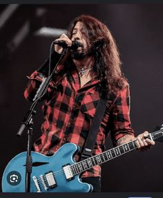 a man with long hair holding a blue guitar and singing into a microphone on stage