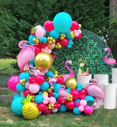 a bunch of balloons that are on the ground in front of a wall with flamingos and pineapples