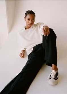 a woman is sitting on the floor wearing black pants and a white sweater with her hand in her pockets