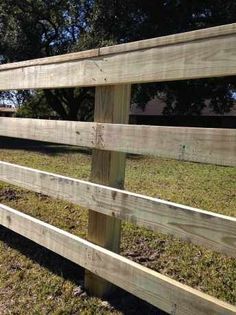 a wooden fence with grass and trees in the background