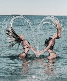 two women in the water holding hands and splashing them with their hair as they stand back to back