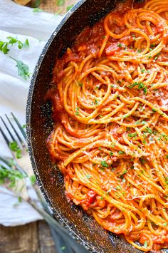 a skillet filled with spaghetti and sauce on top of a wooden table next to a fork