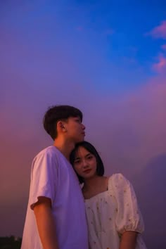 a man and woman standing next to each other under a blue sky with clouds in the background