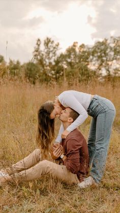 a man and woman kissing while sitting in the grass