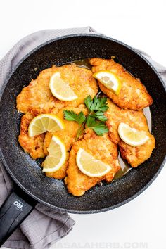 fried chicken with lemons and parsley in a skillet on a white surface