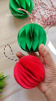 someone is holding two origami balls in their hand, one red and the other green