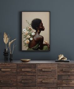 an african woman with flowers in her hair is framed on the wall above a dresser