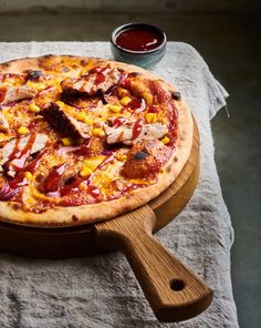 a pizza sitting on top of a wooden cutting board next to a bowl of ketchup