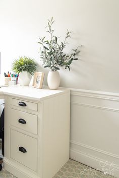 a white desk with two drawers and a potted plant next to it on top