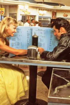 a man and woman sitting at a table in front of each other with menus on them