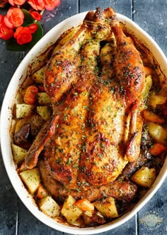 a roasted chicken with potatoes and carrots in a white dish