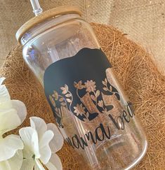 a glass bottle with an elephant on it sitting next to some white flowers and straw