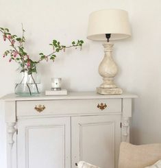 a white cabinet with flowers on top and a lamp next to it