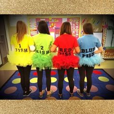 three girls in colorful shirts and tutu skirts looking at something on the wall behind them