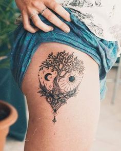 a woman's thigh with a tree and moon tattoo on her left side, next to a potted plant