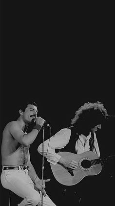 two shirtless men singing into microphones while playing guitar and singing on the stage