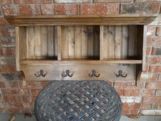 a wooden shelf with hooks on it next to a brick wall