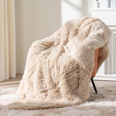 a chair covered in a fluffy blanket on top of a white rug next to a window