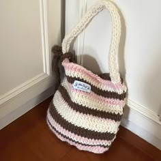 a crocheted purse sitting on the floor next to a white door with a brown and pink handle