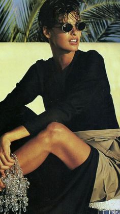 a woman sitting on top of a white couch wearing sunglasses and a black shirt dress