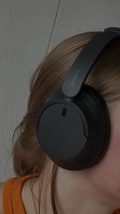 a woman with headphones on her ears is looking down at the wall behind her