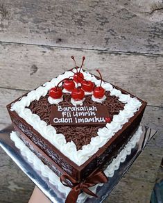 a chocolate cake with cherries on top is being held up by someone's hand