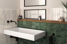 a white sink sitting under two mirrors next to a green tiled bathroom wall with black faucet