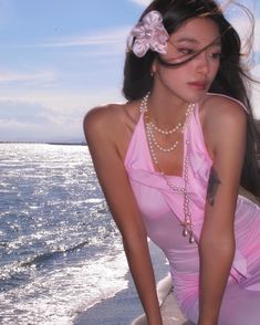 a beautiful young woman in a pink dress standing on the edge of a body of water