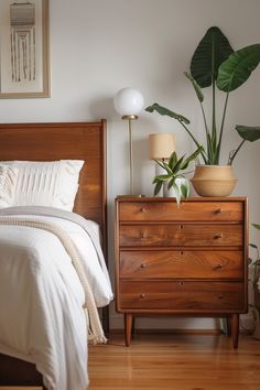 a bedroom with a bed, dresser and potted plant on the side table in front of it