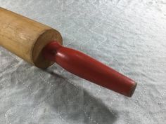 a wooden rolling pin laying on top of a white cloth covered tablecloth with a red handle