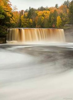 a large waterfall with fall colored trees in the background