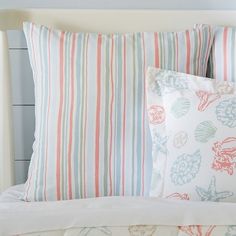 a bed topped with lots of pillows next to a white headboard and night stand