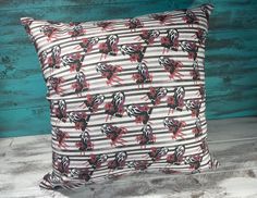 a striped pillow with red and black flowers on it, against a teal wood background