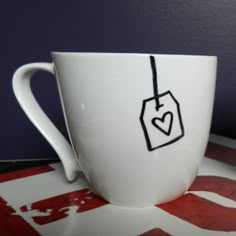 a white coffee cup with a tag on the side and a heart drawn on it