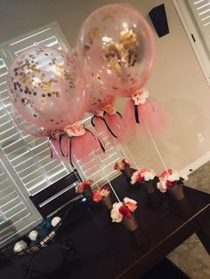 three balloons with gold confetti and pink flowers on them sitting on a table