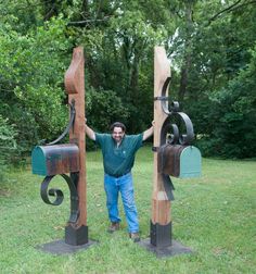 a man standing next to two wooden mailboxes in the middle of a field