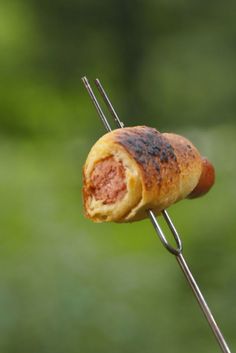 a hot dog on a stick is being held by someone's hand with a grill