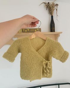 a baby sweater hanging on a rack next to a vase with dried flowers in it