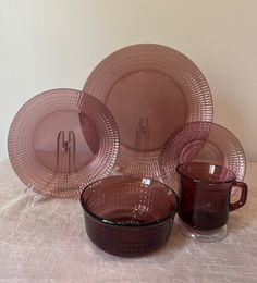 a set of pink glass plates and cups on top of a tablecloth covered table