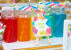 colorful drinks are lined up on a table with paper straws and signs in front of them