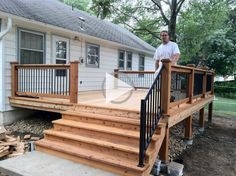 a man standing on top of a wooden deck next to a house with stairs and railings