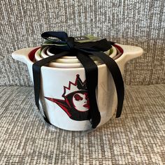 a white tea pot with a black ribbon tied around it on top of a couch