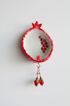 a red and white bowl with some fruit hanging from it's side on a hook