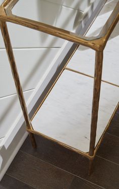 a glass and brass side table on the floor