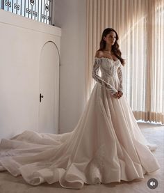 a woman in a wedding dress is standing by a window with her hands on her hips