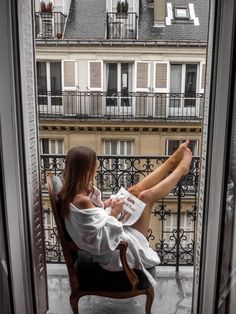 a woman sitting in a chair on top of a balcony looking out at the city