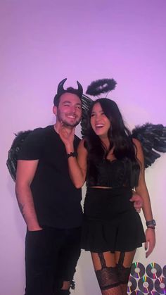 a man and woman posing for a photo in front of a wall with angel wings